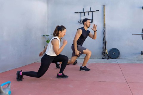 Two fitness professionals are demonstrating perfect lunge form in an outdoor gym area, showcasing