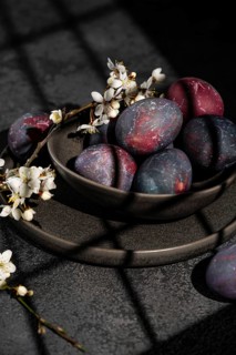 Vibrant, naturally dyed Easter eggs rest in a dark ceramic bowl, adorned with delicate cherry