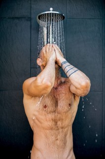 A man enjoys a refreshing shower under a modern showerhead, with water cascading over his body as