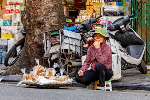Elderly woman sits by her bread stall on the pavement and seems to be on a quiet break, woman