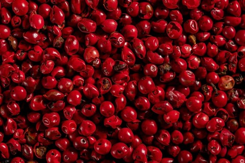 Densely packed red peppercorns with a vibrant color and some with visible stems, showing varied