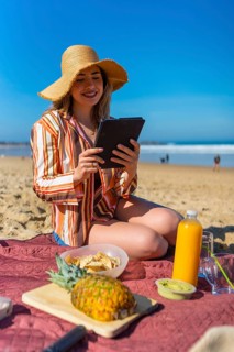 Young woman sitting on a picnic blanket on a sunny beach, enjoying a relaxing vacation while