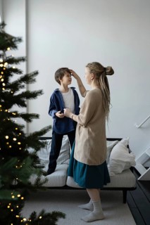A mother lovingly tends to her child's hair as they stand by a Christmas tree adorned with glowing