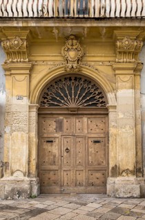 Old decorated stone portal with weathered wooden door and yellowish facets, old town centre of