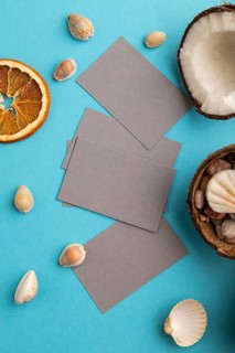 Gray paper business card with coconut and seashells on blue pastel background. Top view, flat lay,