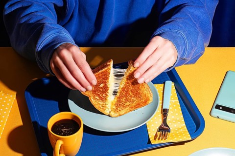 From above, a close-up shot of hands pulling apart a grilled cheese sandwich, revealing melted