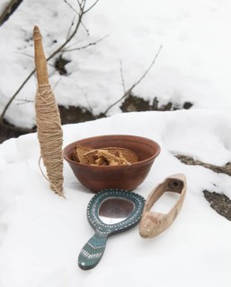 Spindle, mirror and clay plate with bread in the snow. Pagan altar, offering of gifts. Still life
