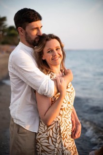 A couple embraces on a scenic Italian beach at sunset, exuding love and serenity. The idyllic
