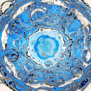 Rising carbon dioxide bubbles in a full water glass with a blue bottom seen from above, detail,