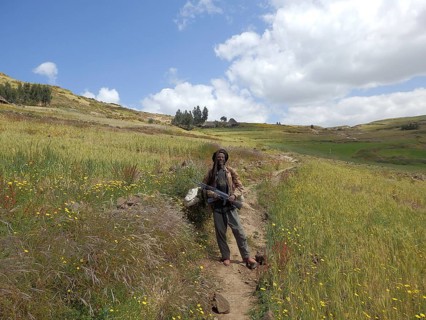Man standing smiling with a rifle, Kalashnikov in a flower-rich field surrounded by rolling hills,
