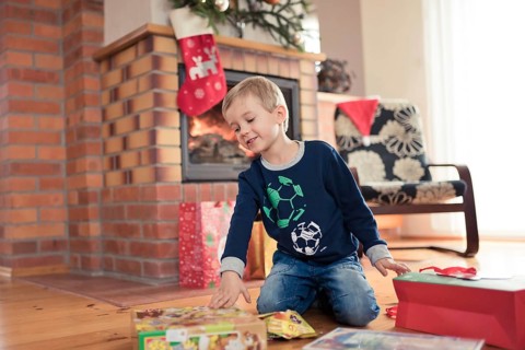 5 years old boy in front of the fireplace is happy with Christmas gifts in Tymowa, Poland