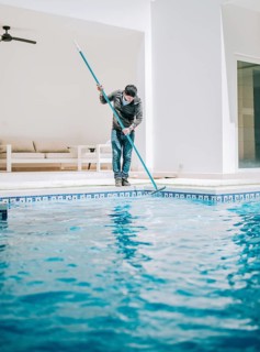 Male worker cleaning a home swimming pool with special brush. Home pool cleaning with wall brush