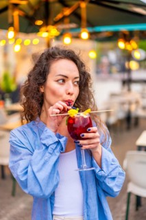 Vertical portrait of a beauty adult caucasian woman using straw drinking cocktail in a terrace