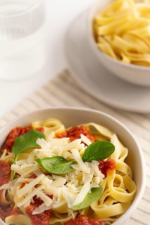 A close up of spaghetti topped with vibrant tomato sauce, grated cheese, and fresh spinach in a