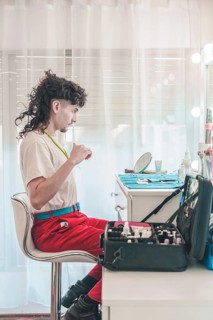 Young non-binary make-up artist sitting comfortably at home, combing hair and preparing for work in
