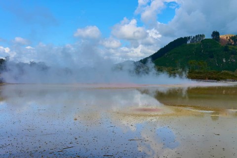 A steaming lake with surrounding mountains and clouds in the sky, Champagne Pool thermal lake,