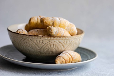 From above, a rustic ceramic bowl filled with freshly baked homemade croissants is placed on a