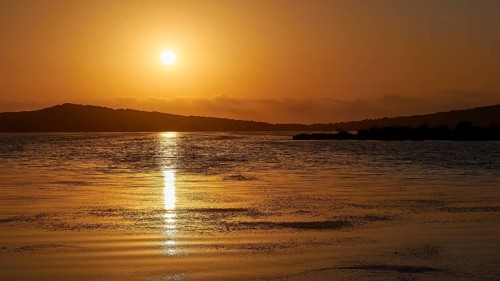 Sunset over calm sea with golden hues and distant hills, Gialova lagoon, protected wetland, bird