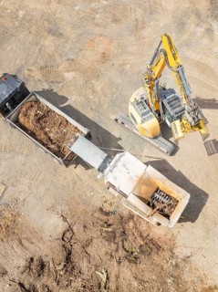 Aerial view of an excavator loading soil into a lorry on a construction site, demolition site,