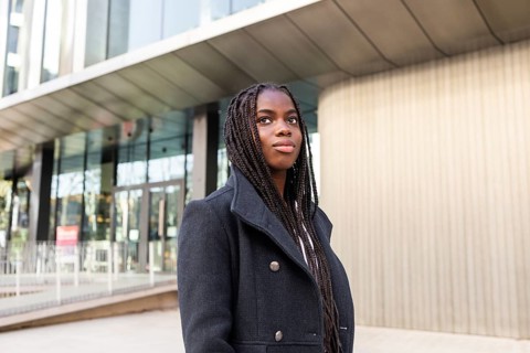A young professional African American businesswoman with long braids outdoors, looking away