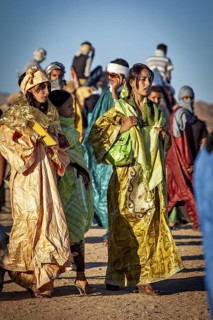 People in colourful traditional dress stand together in a desert landscape, veiled woman at the