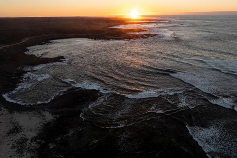 Aerial image capturing a serene sunset over Popcorn Beach in Fuerteventura, with waves gently