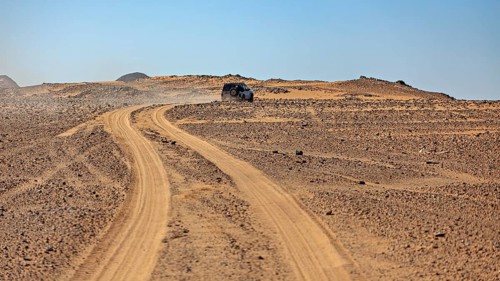 An off-road vehicle on a dusty road in a vast, barren desert landscape, off-road by car through the