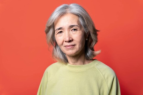 Portrait of an Asian senior woman with gray hair, wearing a light green sweater. She stands