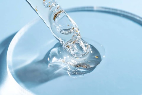 Macro shot of a cosmetic dropper with clear golden flakes floating in a skincare serum against a