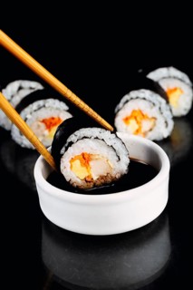 Sushi rolls are elegantly held with chopsticks, dipped into soy sauce, set against a dramatic dark