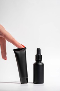 Cropped unrecognizable female hand with red manicure points at black cosmetic packaging against a