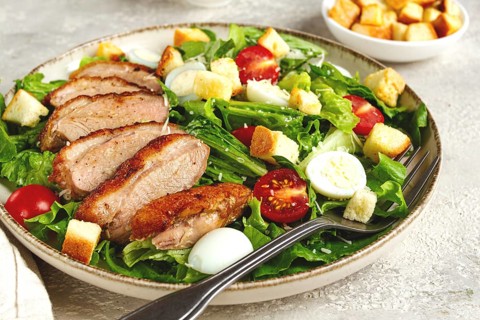 Caesar salad, with duck breast, on a light plate, on a light background, homemade, no people
