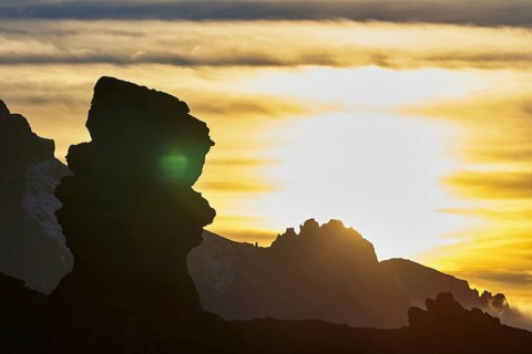 Rock silhouette against golden sunset, unique light show in dramatic scenery, Teide, Parque