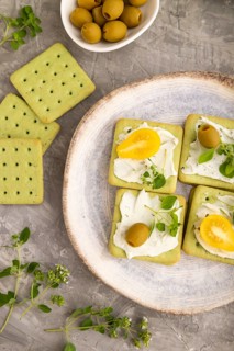 Green cracker sandwiches with cream cheese and cherry tomatoes on gray concrete background. top