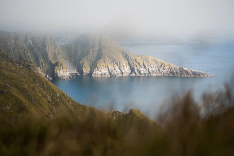 A serene coastal scene in Norway, showcasing mist-covered cliffs surrounded by calm ocean waters