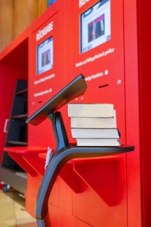 A modern robotic arm holds books in front of red return machines, interactive guided tours by