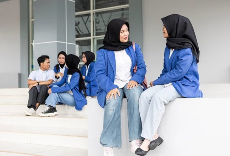 Asian Muslim students wearing hijabs and casual attire engage in conversation while sitting