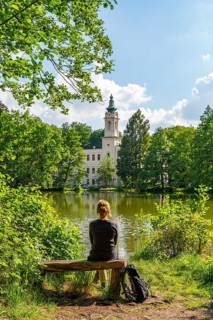 Woman hiking sitting on a bench with a view of Dammsmühle Castle at the mill pond, Schönwalde,