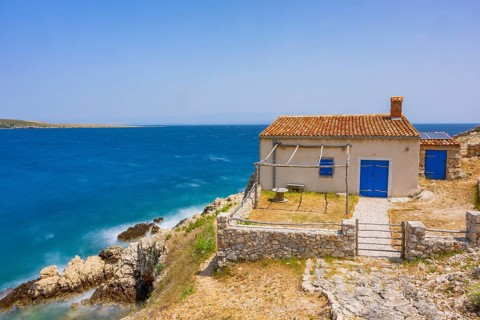 Small house in Koromacna Bay built on the rocks above the sea with a view of the sea on a sunny day