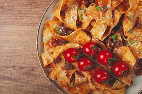 Pappardelle pasta with bolognese sauce, topped with parmesan cheese and cherry branch, homemade, no