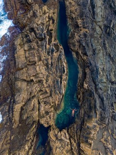 Top view of an unrecognizable woman floating peacefully in a natural pool amid rugged cliffs at