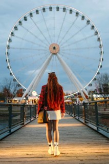 Back view of unrecognizable woman with long red hair walking toward a lit Ferris wheel in Montreal,