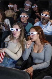 Group of diverse friends wearing 3d glasses enjoying a movie at the cinema, eating popcorn and