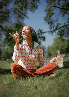 A cheerful woman sits on the grass, embracing the beauty of nature with a refreshing bottle of