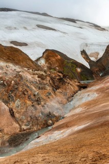 Steaming stream between colourful rhyolite mountains and snowfields, Hveradalir geothermal area,