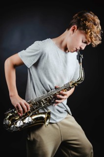 A teenage boy passionately playing a saxophone in a dimly lit studio, highlighted against a black