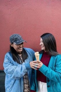 A Latin lesbian couple shares a joyful moment while enjoying an ice cream against a vibrant red