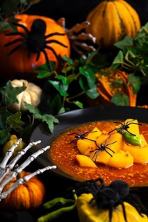 Halloween still life, goulash decorated with artificial spiders, pumpkins and green leaves,