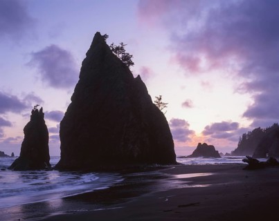 Stunning coastal scene featuring tall, jagged sea stacks silhouetted against a colorful sunset sky,