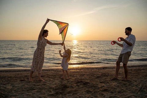 A family enjoys flying a kite on a picturesque Italian beach at sunset. The serene sea and warm